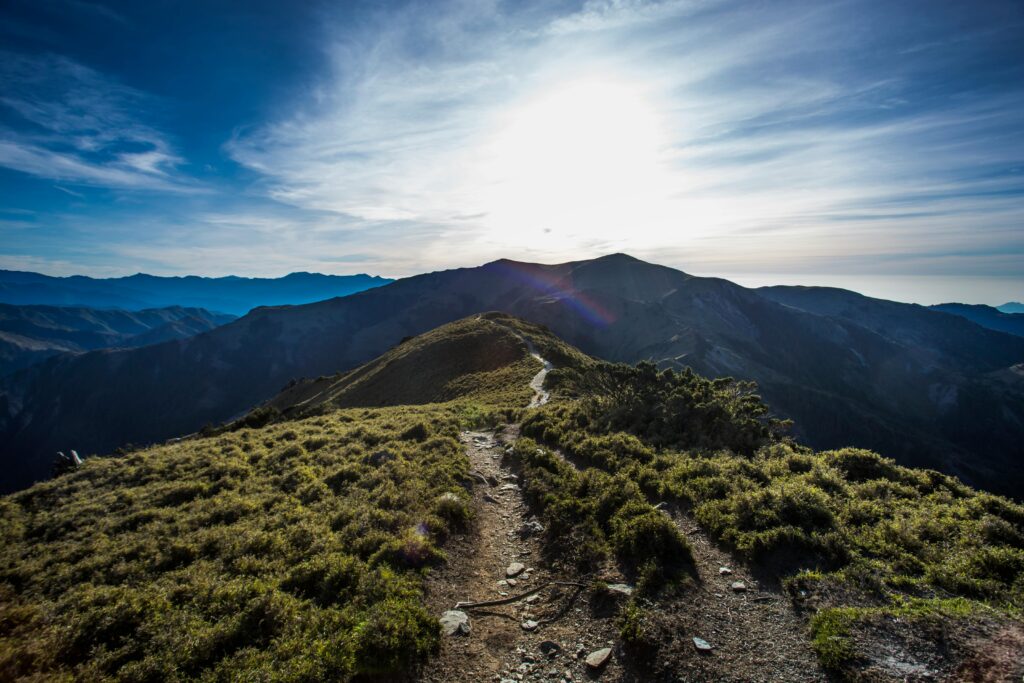 A breathtaking mountain trail with grassy peaks under a bright blue sky at sunrise.